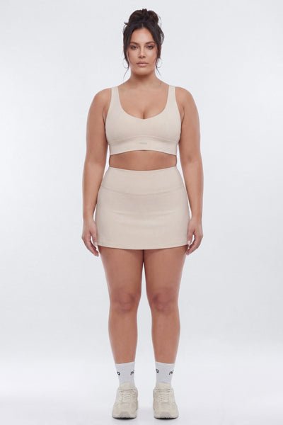 Woman wearing a beige sports bra and skirt set on a white background