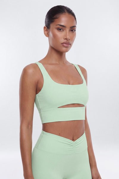Woman wearing a light green sports bra and leggings on a white background