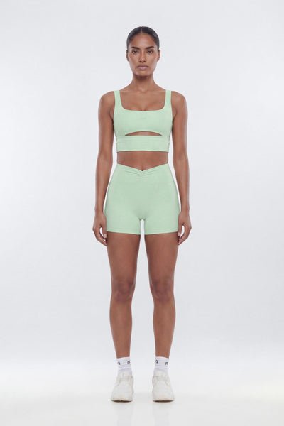 Woman wearing a light green sports bra and shorts set on a white background