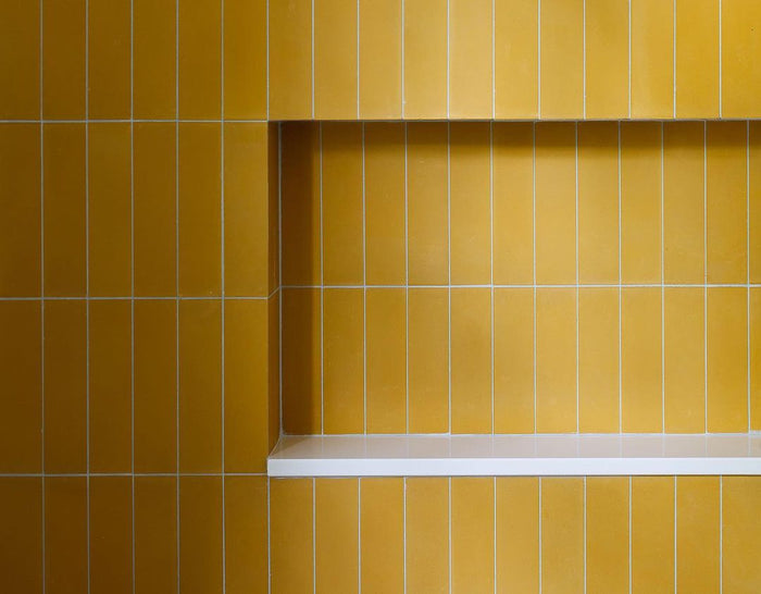 A wall clad in vendor-unknown's Cadmium 2x8 tiles with white grout and a recessed rectangular shelf with a white base—an eye-catching choice for your kitchen backsplash.