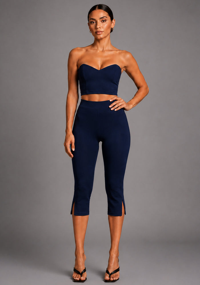 Front image of a model wearing the VSPR Benedetta Strapless Navy Crop Top with a clean semi-V neckline and sculpted strapless silhouette. The design paired with Capri Cropped Navy Trousers, against a grey studio backdrop.