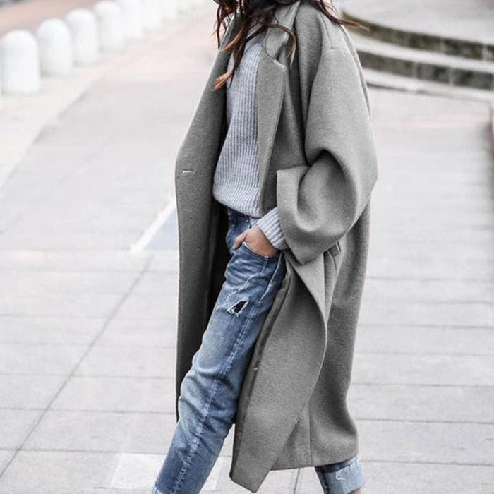 Person wearing a long gray coat over a light blue sweater and jeans on a city street.