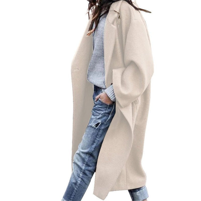 Person wearing a beige coat over a blue plaid shirt and jeans on a white background