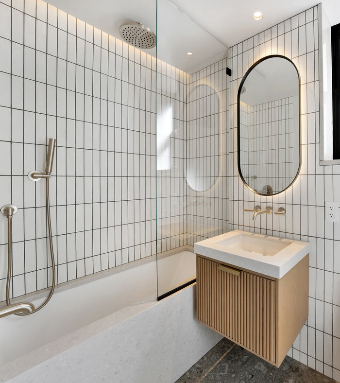 Modern bathroom featuring Cotton 2x8 subway tile by vendor-unknown, a glass shower partition, rainfall showerhead, wall-mounted sink with wood vanity, oval mirror, and recessed lighting.