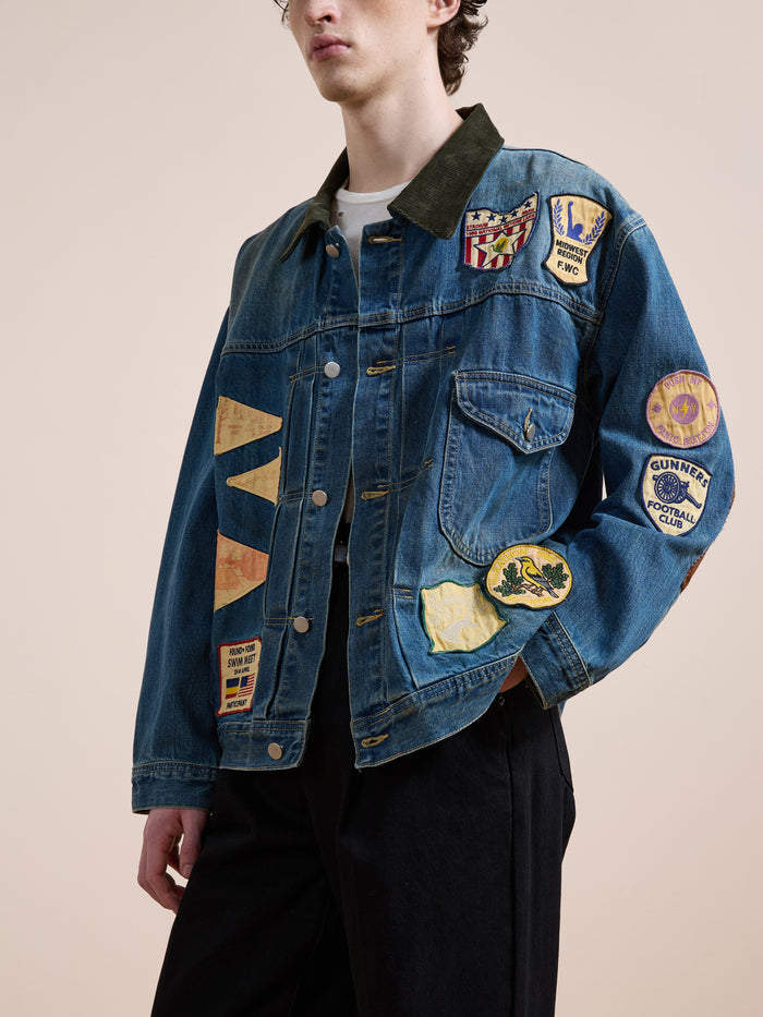 A person wears the FOUND Denim Patchwork Jacket with colorful patches and black pants, standing against a plain background.
