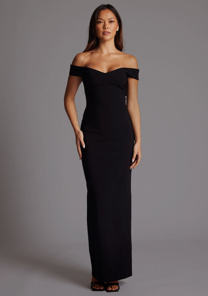 Front image of a model wearing a black maxi dress, featuring off-the-shoulder short sleeves and a dipped back design. The dress feature is the Vesper Holland Sweetheart Neckline Off The Shoulder Maxi Dress in Black