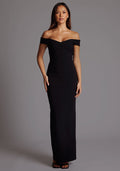 Front image of a model wearing a black maxi dress, featuring off-the-shoulder short sleeves and a dipped back design. The dress feature is the Vesper Holland Sweetheart Neckline Off The Shoulder Maxi Dress in Black