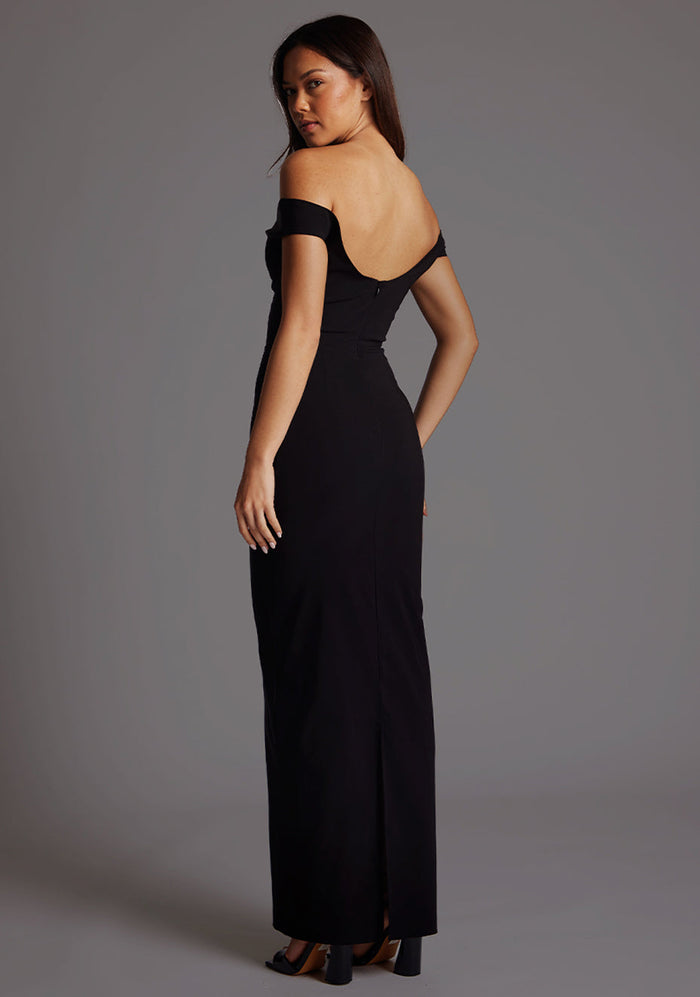 Side back image of a model wearing a black maxi dress, featuring off-the-shoulder short sleeves and a dipped back design. The dress feature is the Vesper Holland Sweetheart Neckline Off The Shoulder Maxi Dress in Black.