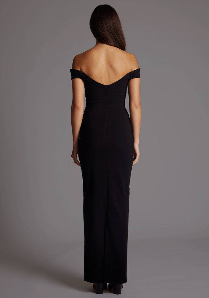 Back image of a model wearing a black maxi dress, featuring off-the-shoulder short sleeves and a dipped back design. The dress feature is the Vesper Holland Sweetheart Neckline Off The Shoulder Maxi Dress in Black.