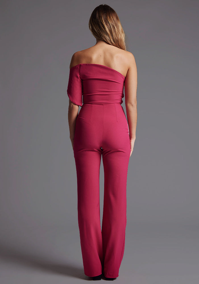 Back image of a model wearing a  with a stunning one-shoulder design and a body-hugging fit that accentuates your curves in all the right places and side zip fastening ensures a seamless look. The design featured is the Vesper Ines One Shoulder Jumpsuit in Raspberry.