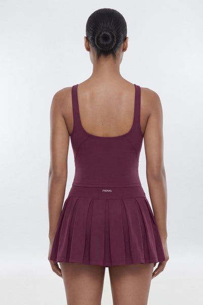 A woman shown from the back wearing a sleeveless athletic dress with a scoop neckline and a pleated skirt, in a deep plum-burgundy color. The brand name 'FING' is visible on the back waistband.