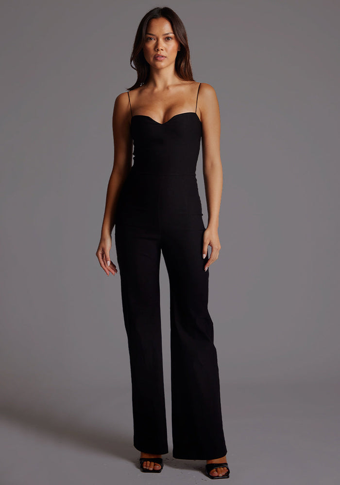 Front image of a model wearing the VSPR Rogan Sweetheart Neck Wide Leg Jumpsuit in Black highlighting the sculpted sweetheart neckline, slender shoulder strap and wide-leg silhouette, standing against a grey studio backdrop.