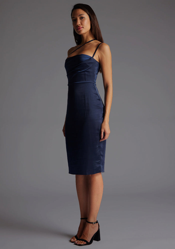 Front quarter image of a model wearing a navy satin midi dress with a straight neckline with a asymmetric strap across front of chest and invisible centre back zip. The design featured is the Vesper Rosalina Navy Satin Midi Dress