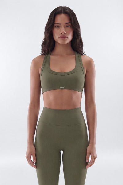 A woman modeling an olive green athletic set consisting of a scoop-neck sports bra and high-waisted leggings